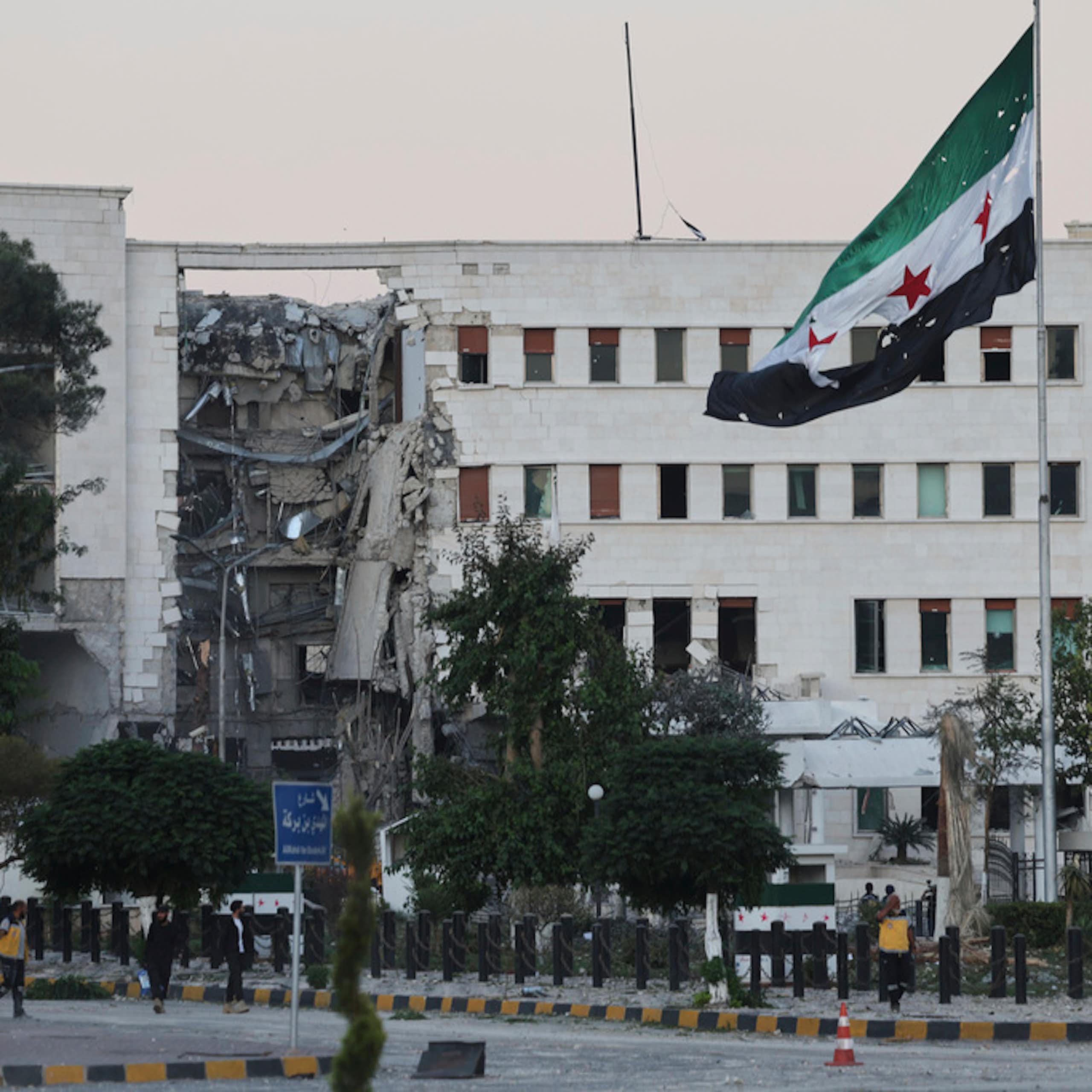 A flag is seen in front of a damaged building.