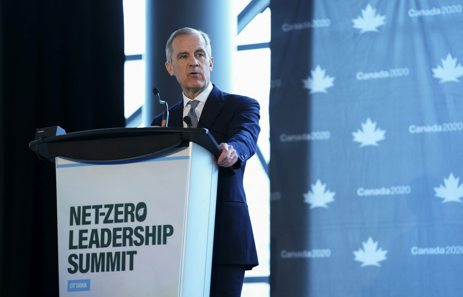 A man with short-grey hair speaks from behind a lectern that reads Net Zero Leadership Summit.