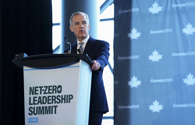 Un hombre con el pelo corto y gris habla a sus espaldas en las que se lee la cumbre del liderazgo neto cero.