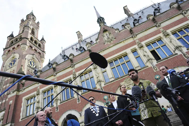 A young man speaks at a news conference in front of a stone court building.