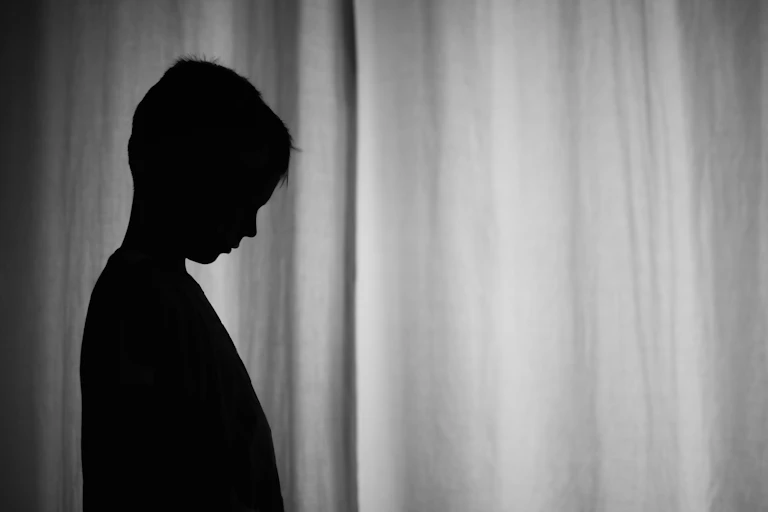 Silhouette of boy standing by curtains