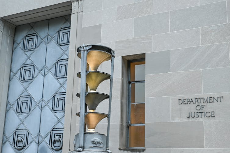 A granite building with a big door, with 'Department of Justice' written on the side.