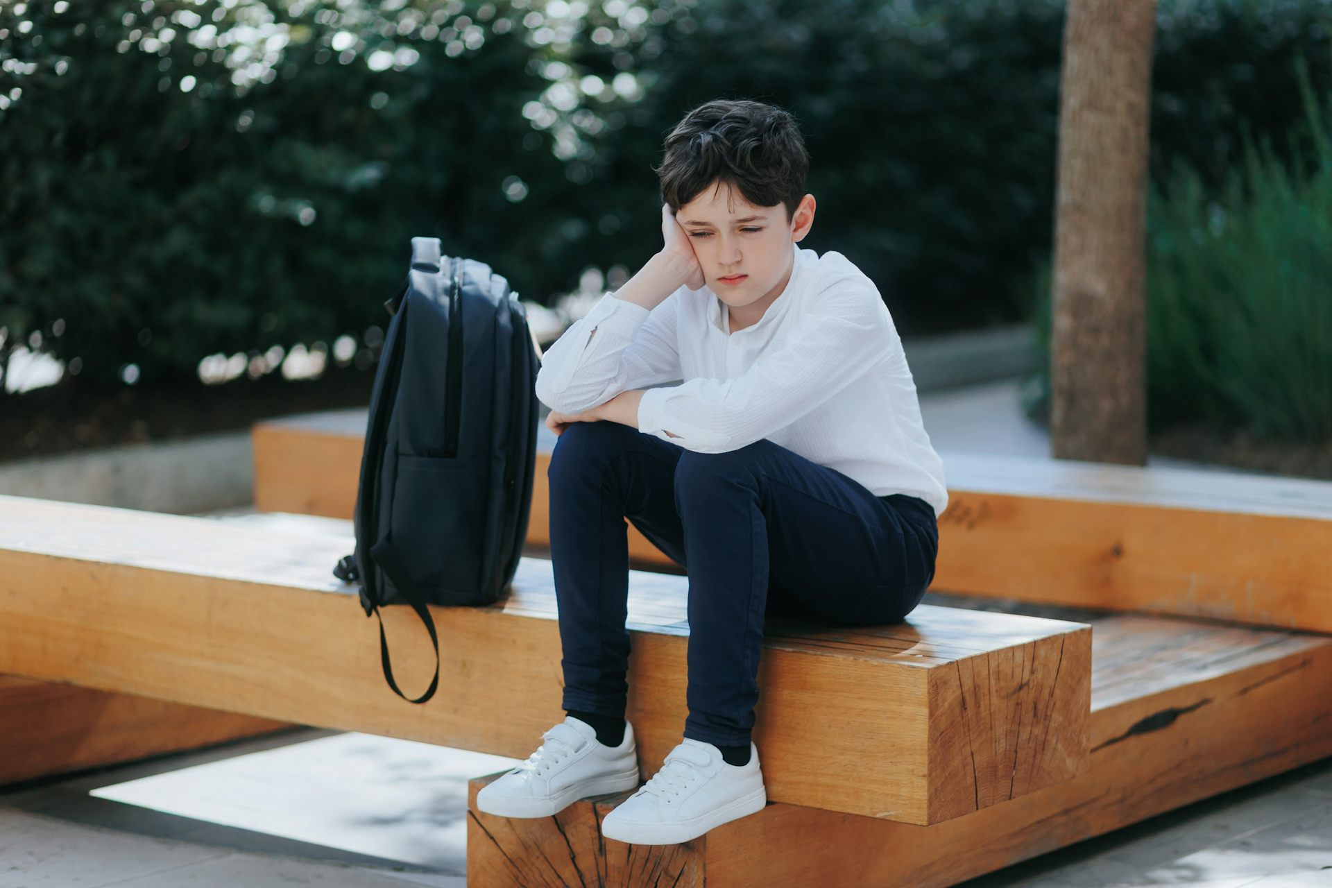 Boy looking sad sat outside alone with school bag