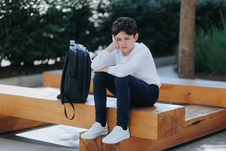 Boy looking sad sat outside alone with school bag