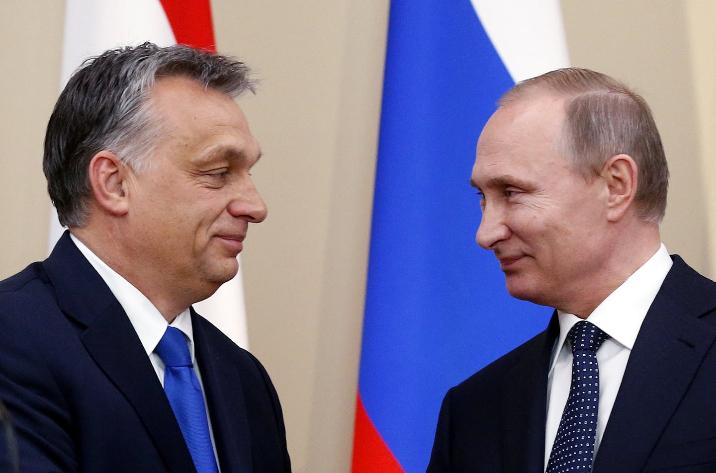 Two men in suits and ties smile at each other.