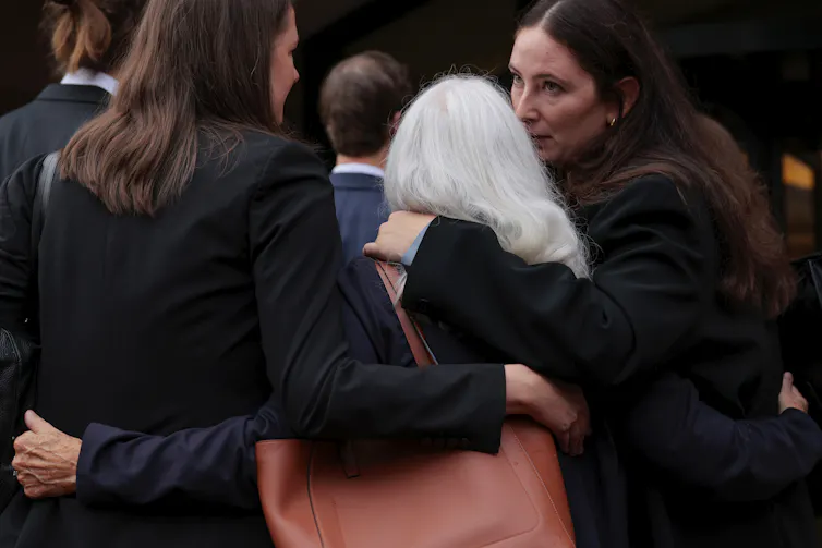 Three women holding each other as they stand outside.