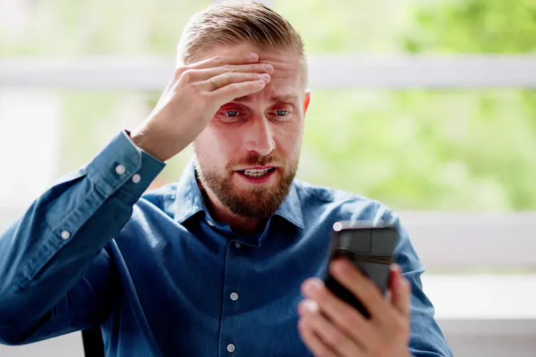 shocked man looking at his phone with his hand on his forehead.