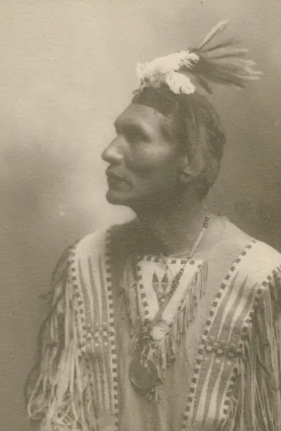 Sepia-toned portrait of man wearing a headdress and traditional Native American clothing.