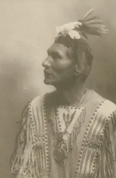 Sepia-toned portrait of man wearing a headdress and traditional Native American clothing.