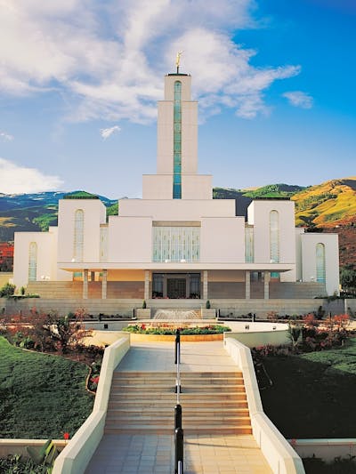 An ornate white building with a tall spire, and green mountains in the background.