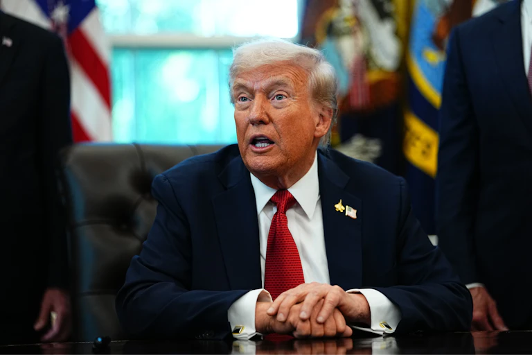 Donald Trump speaks while sitting as a desk in the Oval Office