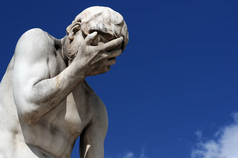 Ancient Greek statue with man looking down, palm over face, looking embarrassed or ashamed