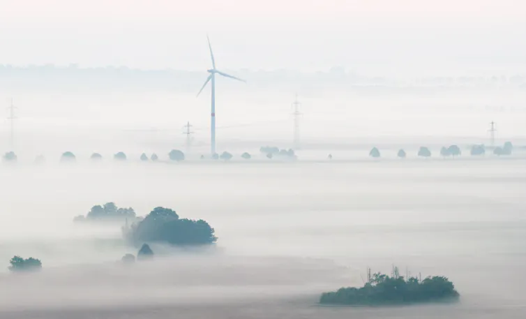A wind turbine stands in a foggy field in France.