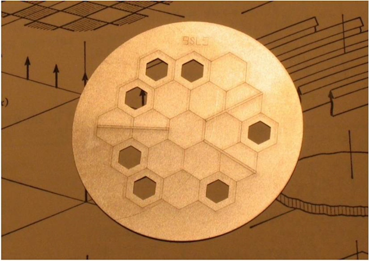 A metal plate with a hexagonal pattern and several hexagon-shaped holes.