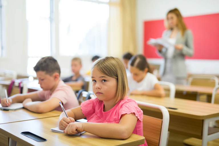 Varios niños escriben en clase, con una niña en primer plano.