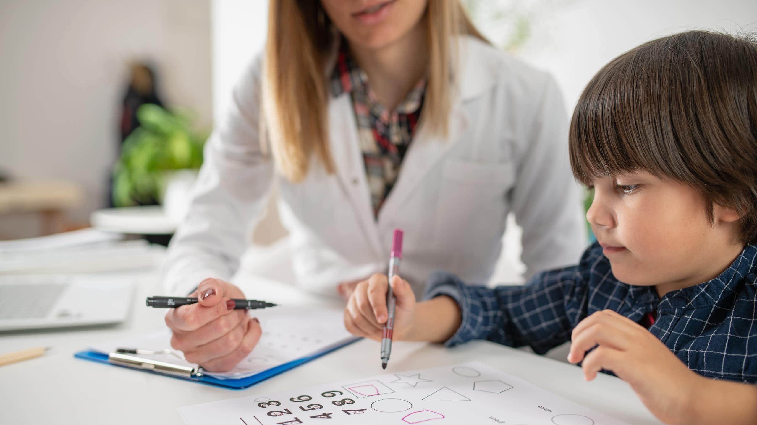 Un enfant passe un test d’évaluation d’intelligence sous le regard d’une femme en blouse blanche.
