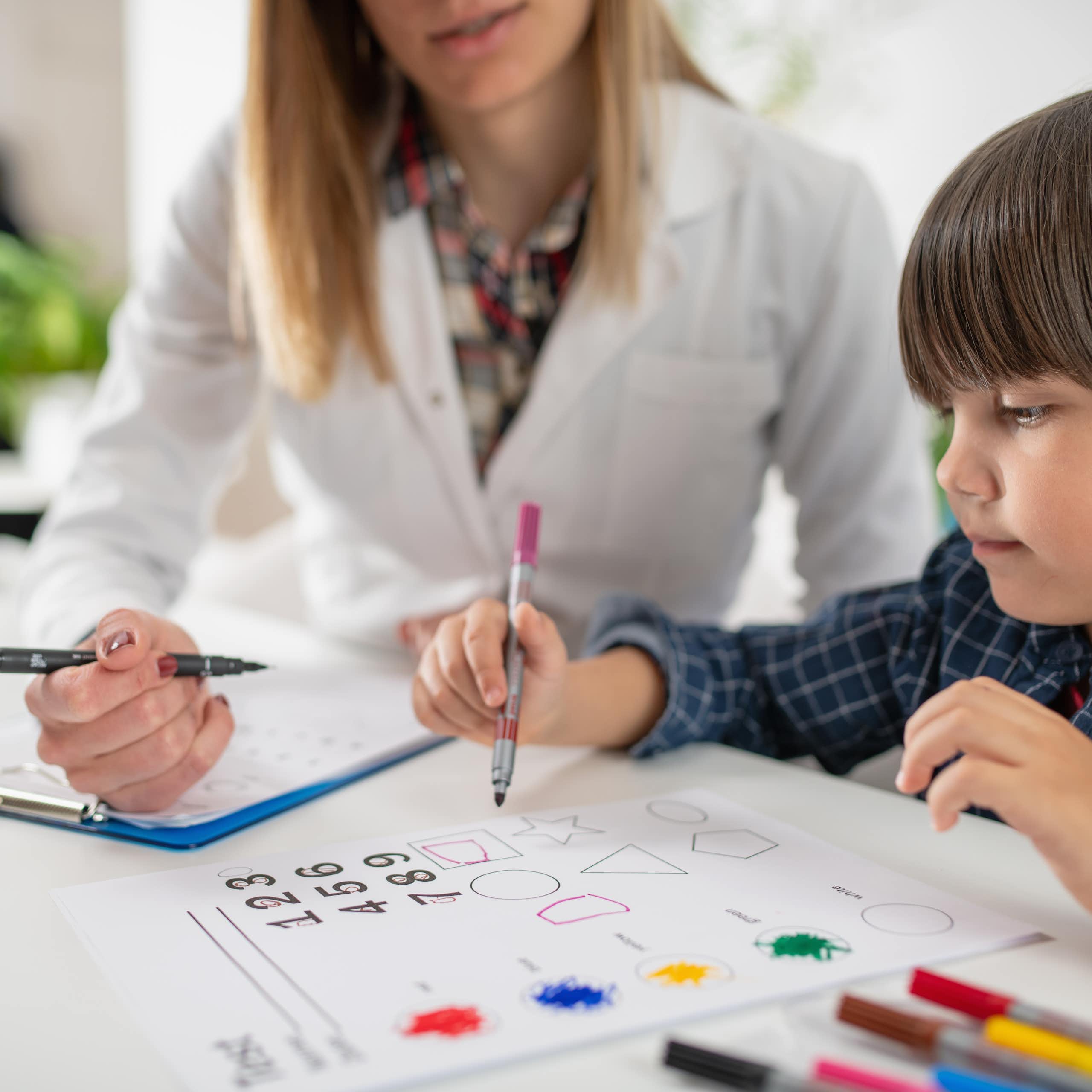 Un enfant passe un test d’évaluation d’intelligence sous le regard d’une femme en blouse blanche.