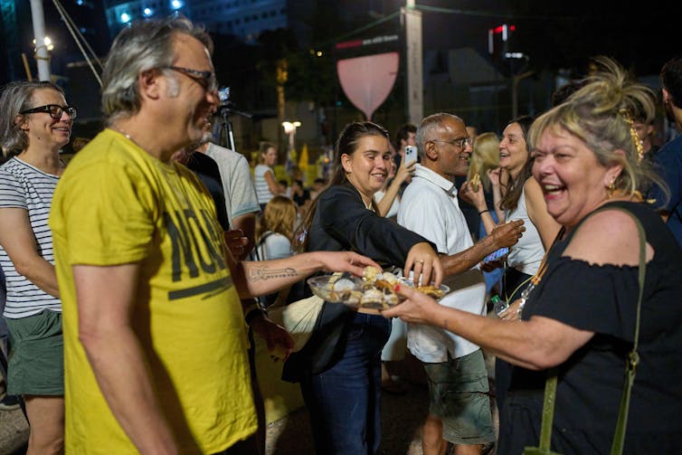 Gaza ceasefire and Donald Trump’s ‘dead cat diplomacy’ 2 A man in a yellow shirt takes a cake from a smiling woman in Tel Aviv.