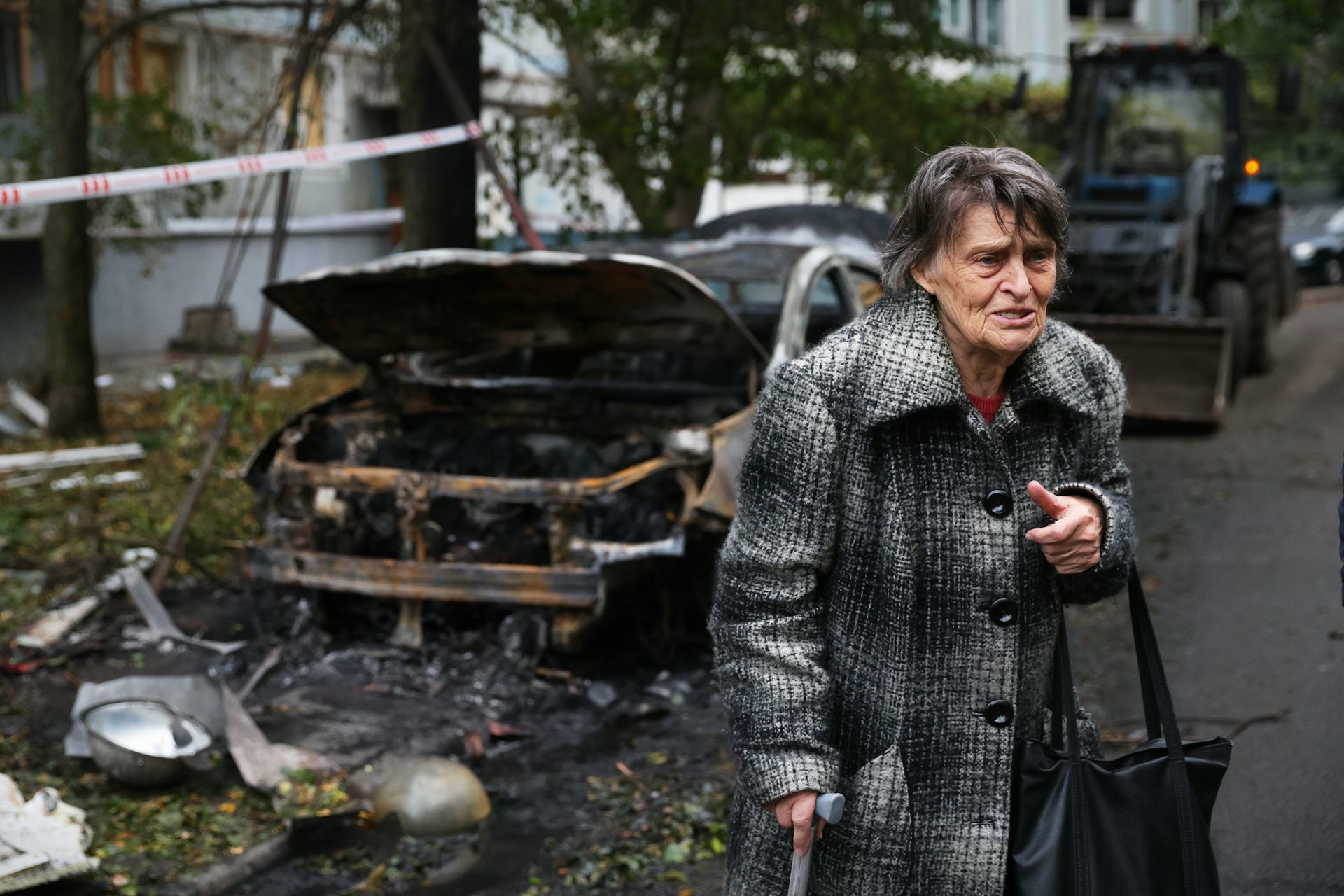 La mujer mayor con abrigos parece revelada junto al coche destruido.