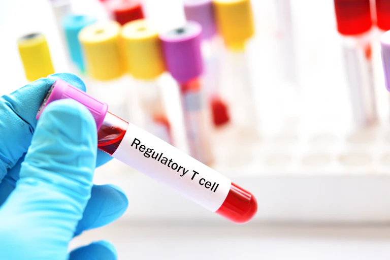 A blue-gloved hand holding a test vial of blood with a sticker that reads 'Regulatory T cell'