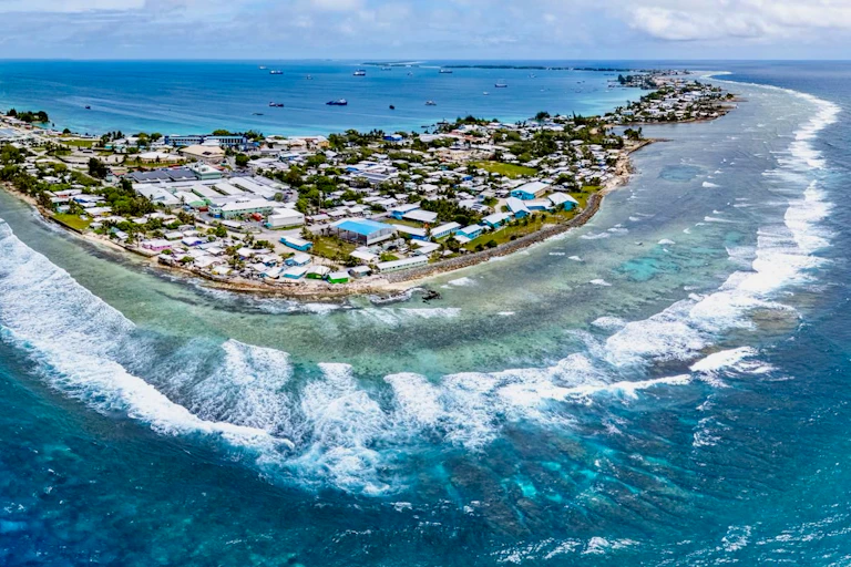 An aerial view of an island filled with buildings. The ocean is a brilliant blue.