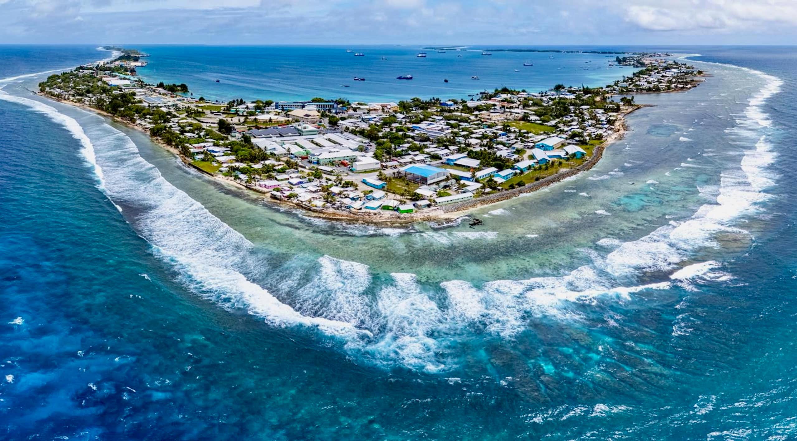 An aerial view of an island filled with buildings. The ocean is a brilliant blue.