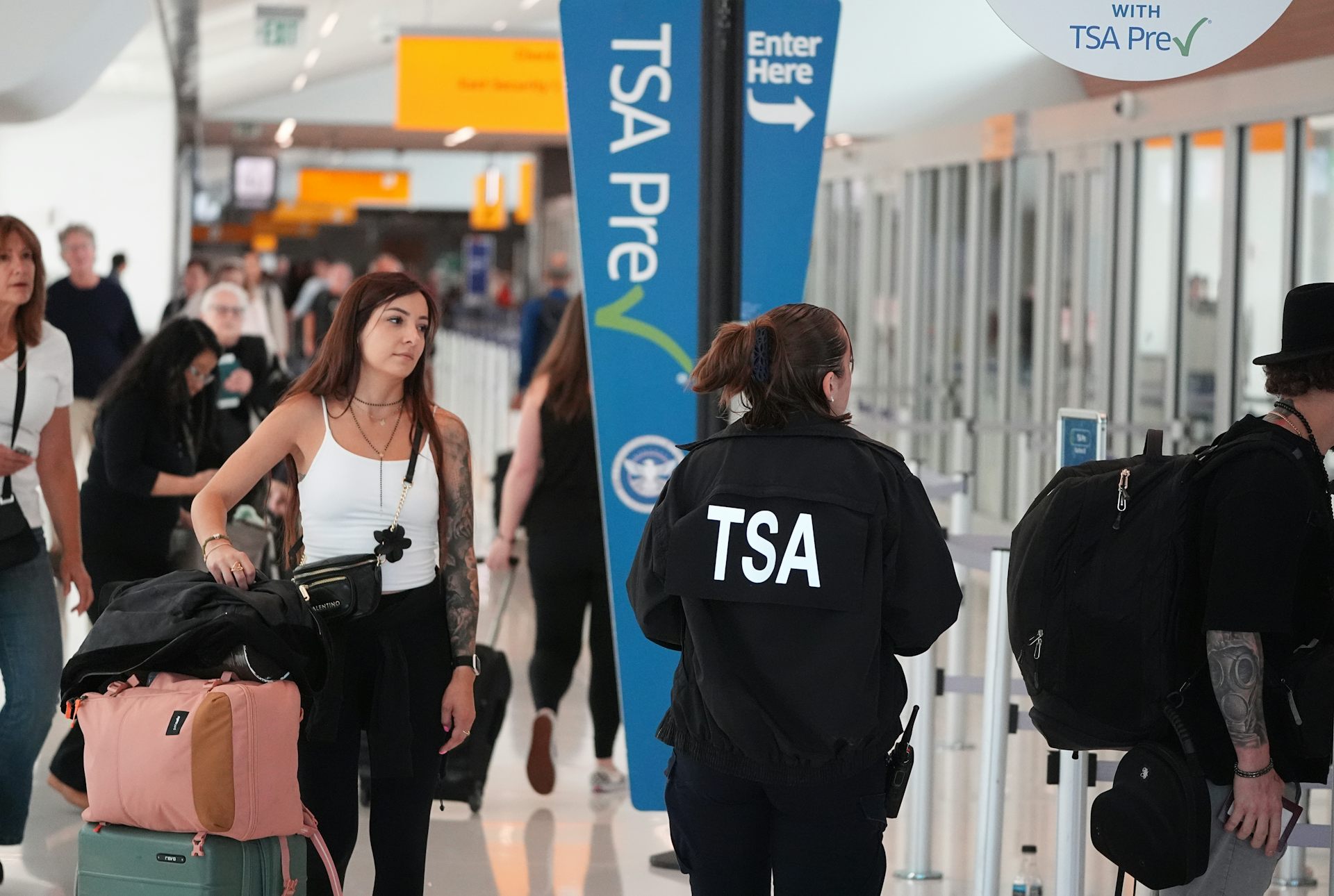 Una persona con una chaqueta negra de la TSA en la espalda guía a los viajeros por el aeropuerto