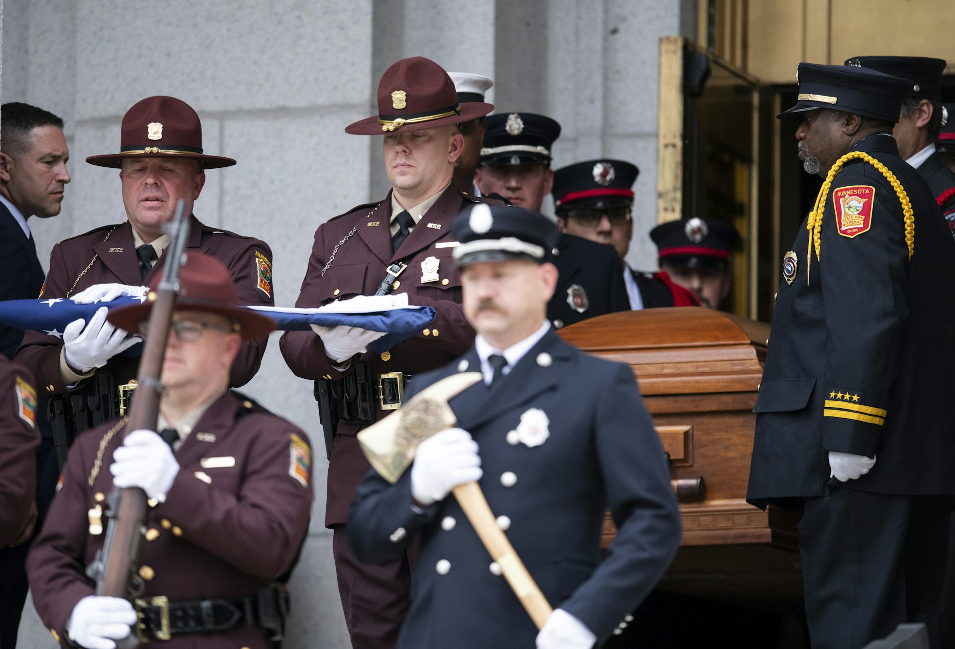 People in uniforms and others carry a casket out of a church.