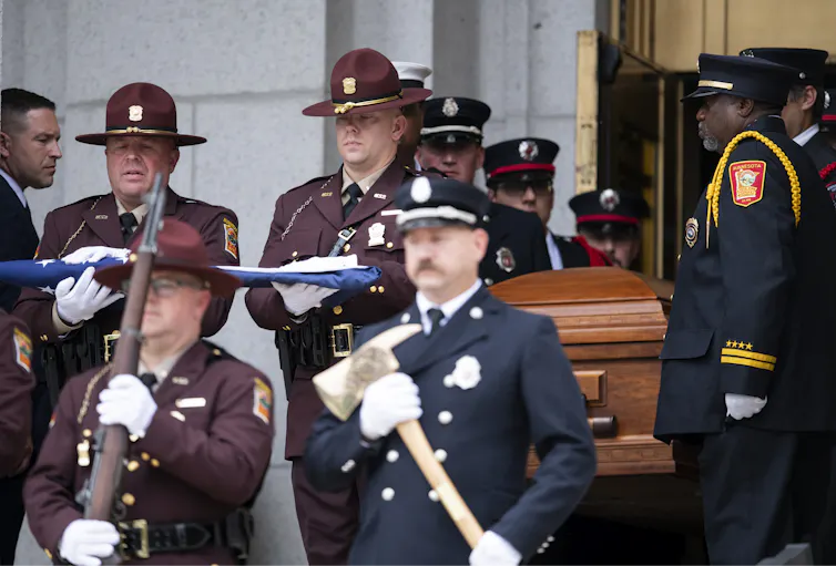 People in uniforms and others carry a casket out of a church.
