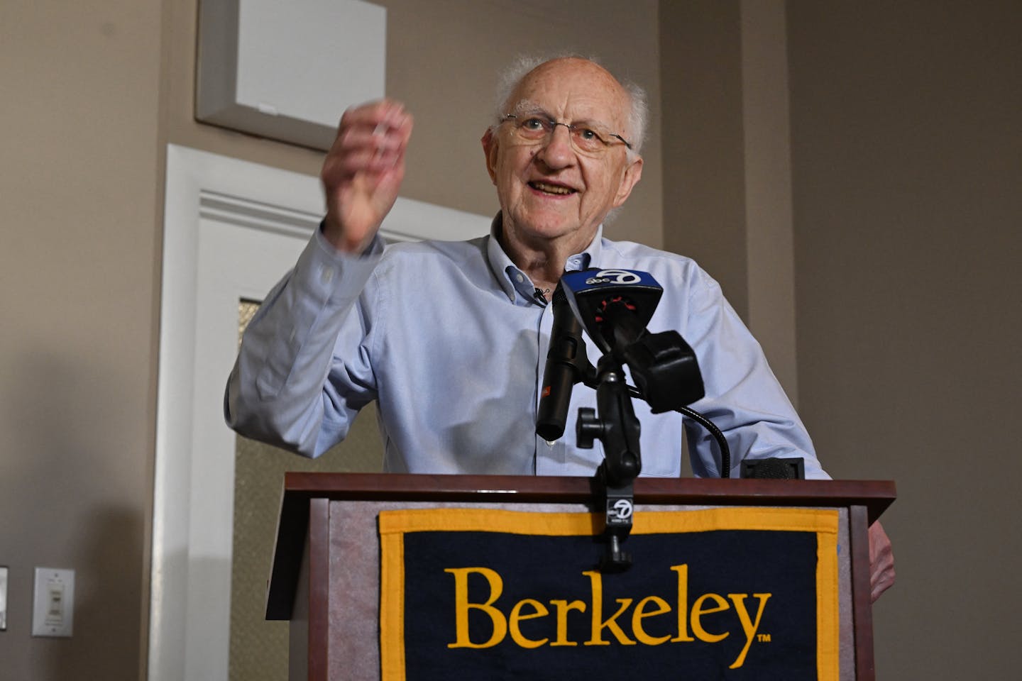 A man speaking at a podium with a 'Berkeley ' sign on it