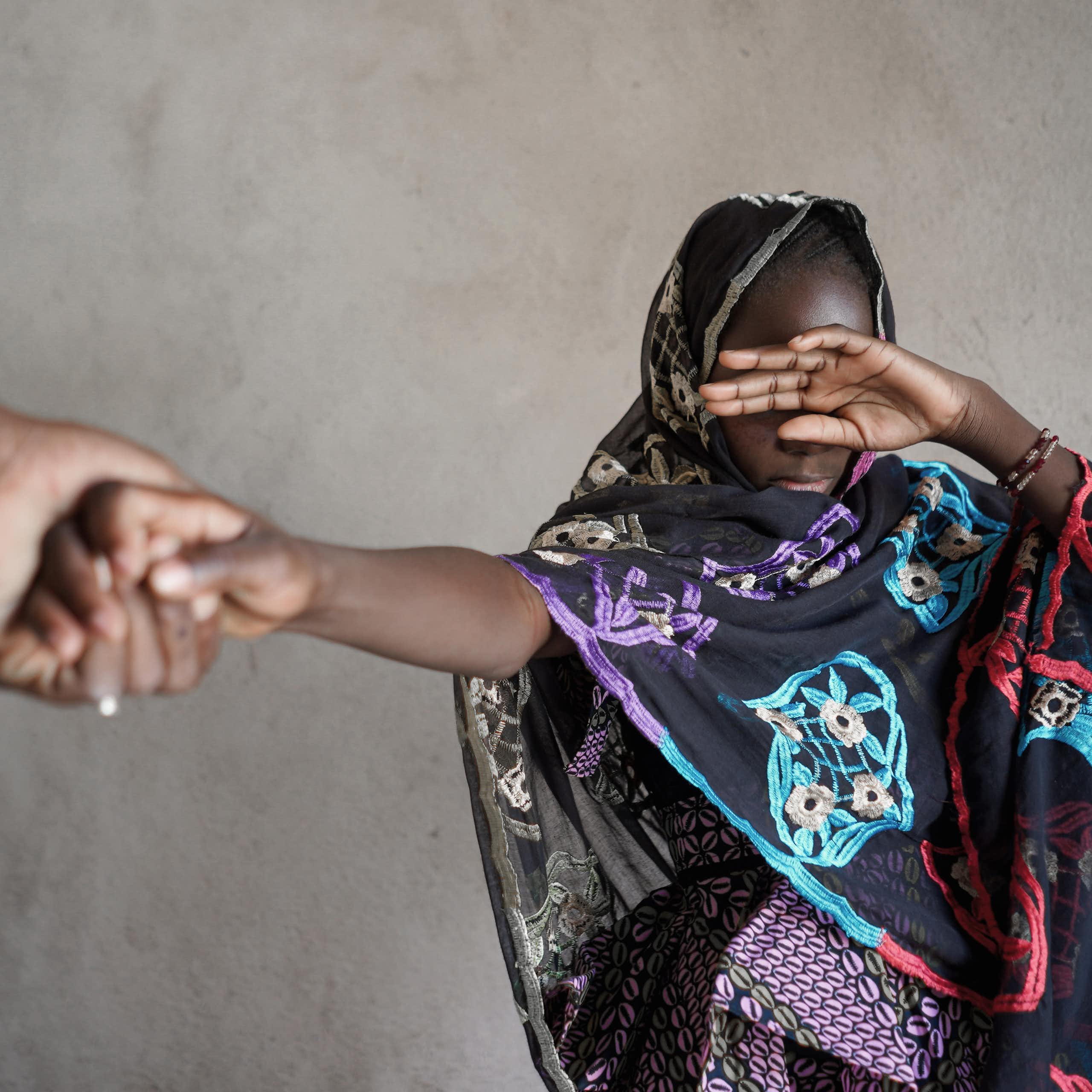 Veiled girl with her hand covering her eyes, pulled by the hand of an adult