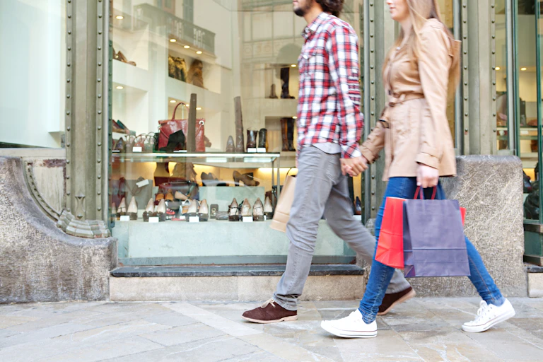 couple walking past a shoe shop holding shopping bags.