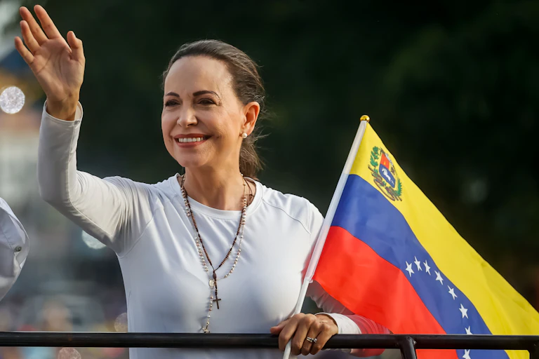 Venezuelan politician Maria Corina Machado smiles and holds a national flag.