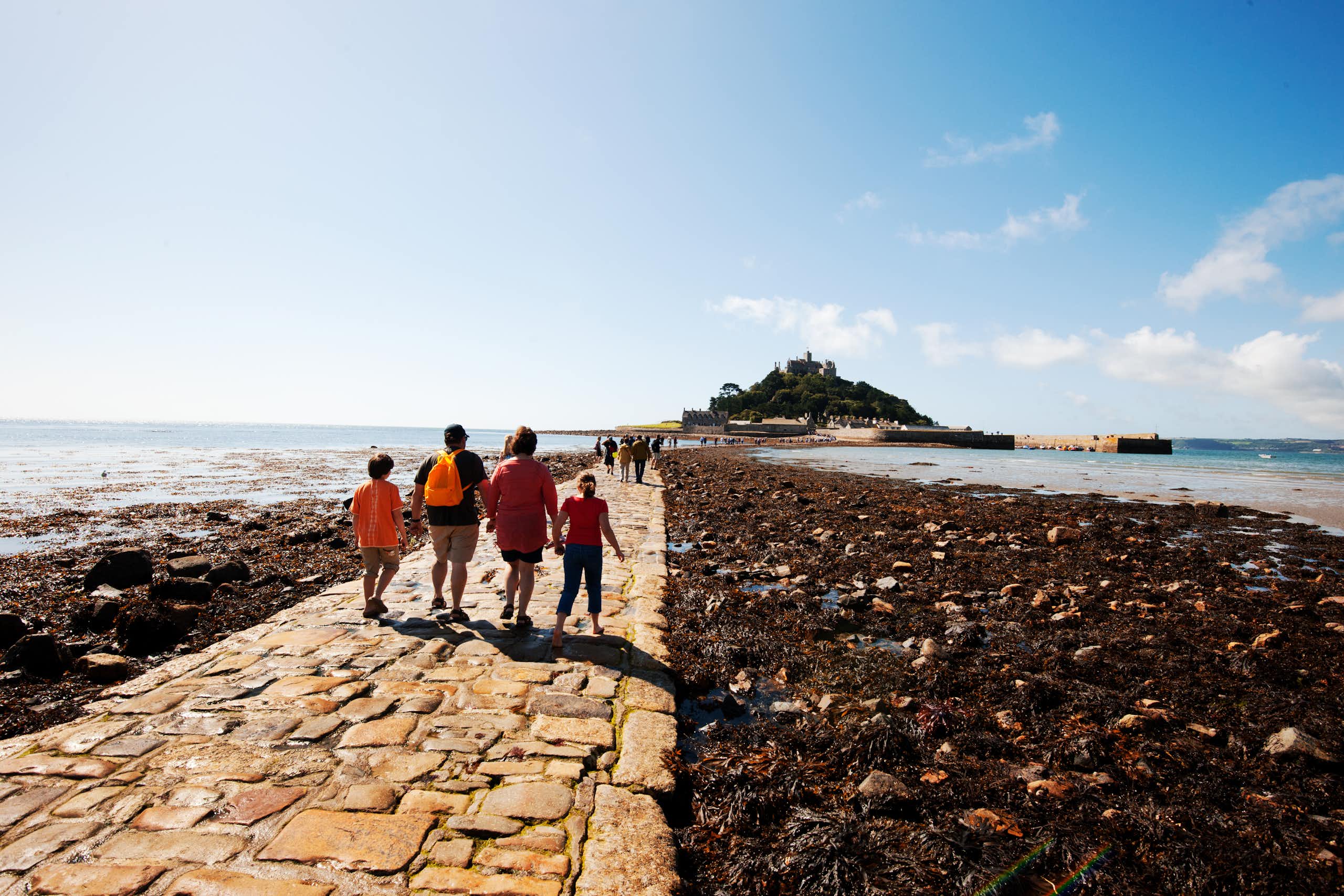 four people walking on causeway to island at low tide, surrounded by sea