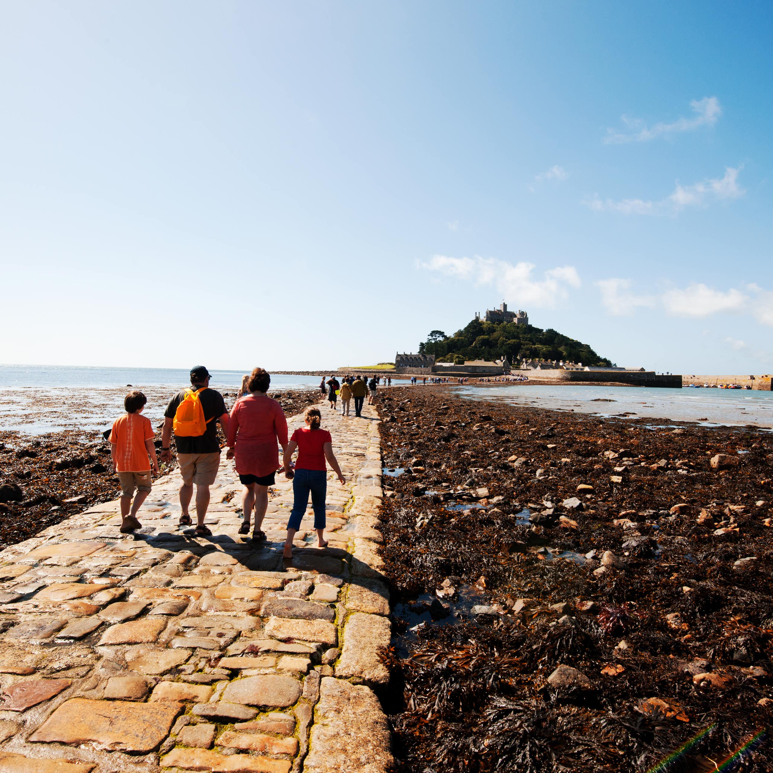 four people walking on causeway to island at low tide, surrounded by sea