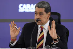 A man with short dark hair and moustache gestures with his hands while speaking.