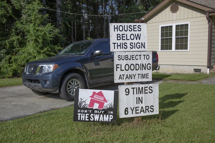 A home with series of signs reading: 'Houses below this sign subject to flooding at any time. 9 times in 6 years.'
