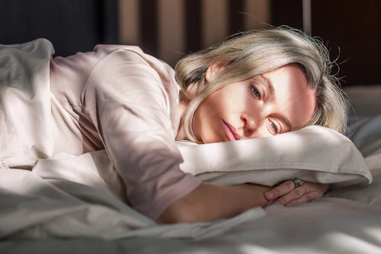 Mulher deitada na cama, acordada, com um ar pensativo.