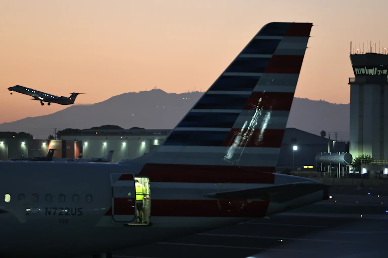 a plane is seen taking off in the distance while in the foreground are a plane on the tarmac and an air traffic control tower.