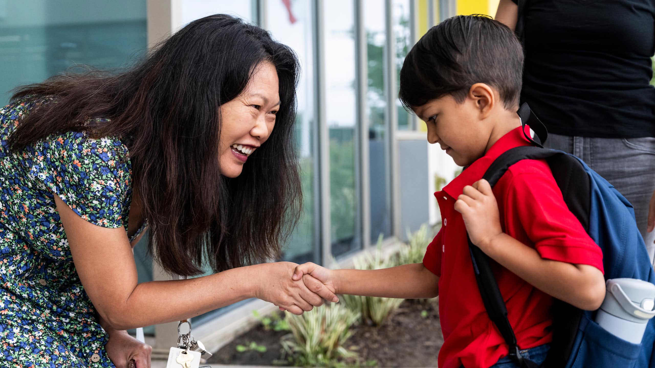 A teacher greets a young student on the first day of school.