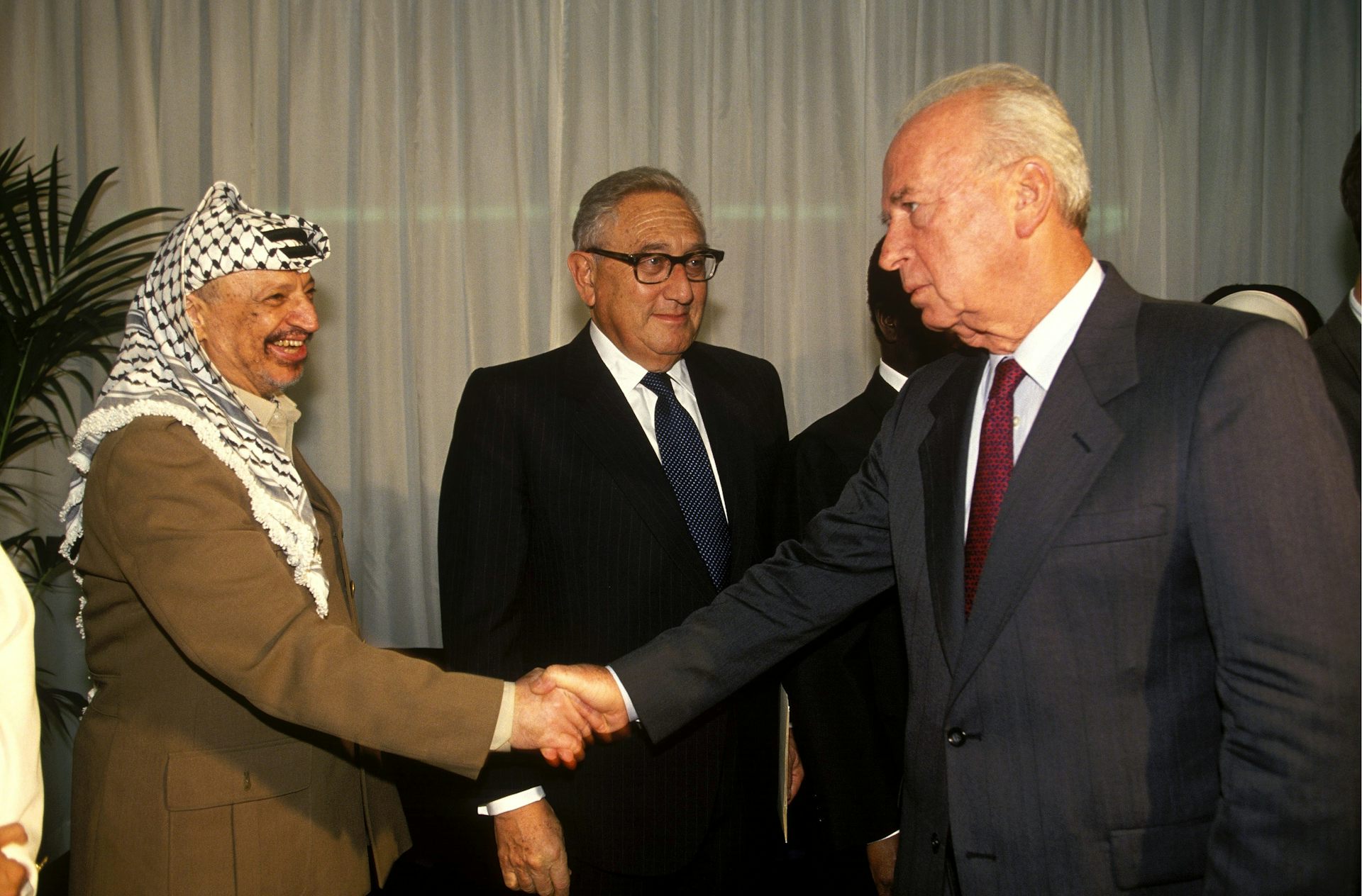 Three men stand, two shaking hands.
