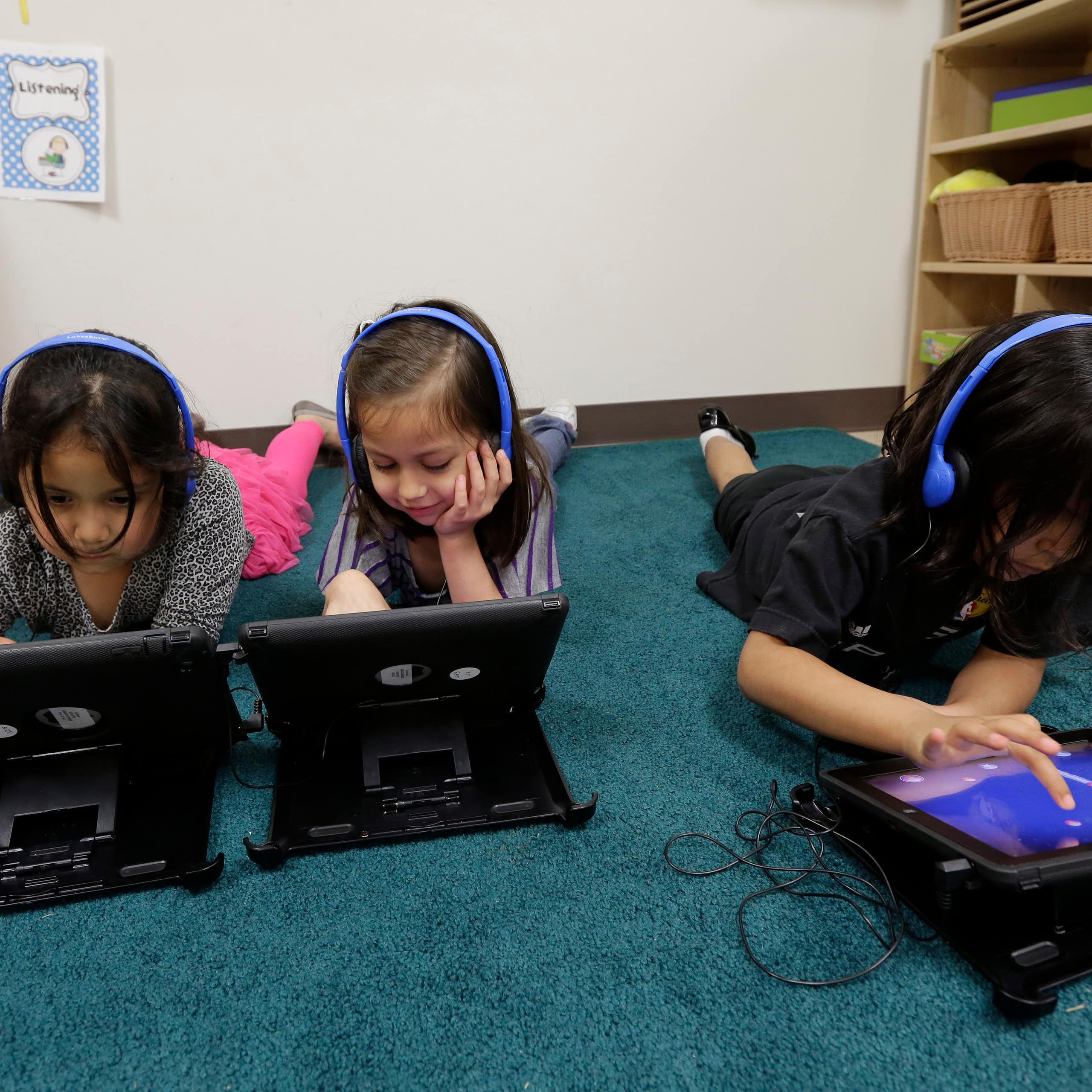 Three young students working on tablets at school.