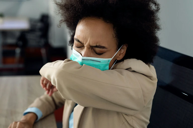 A woman wearing a face mask coughs into the crook of her elbow