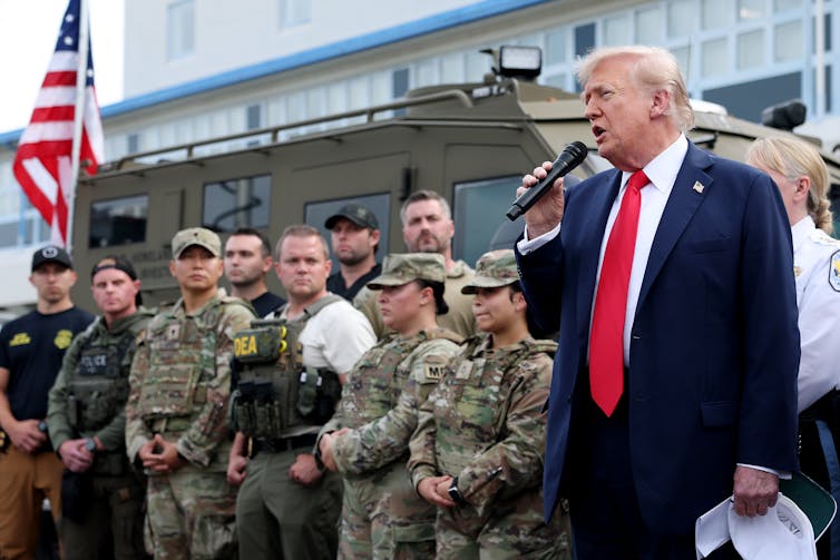 President Trump speaks into a microphone with various uniformed people behind him