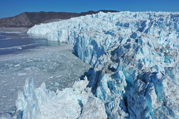 A tall glacier front seen from above shows huge chunks of ice calving off into Disko Bay.