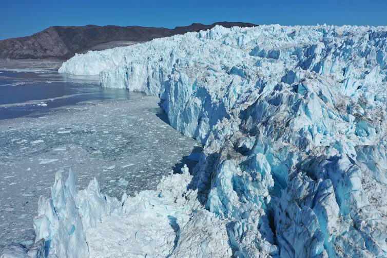 A tall glacier front seen from above shows huge chunks of ice calving off into Disko Bay.