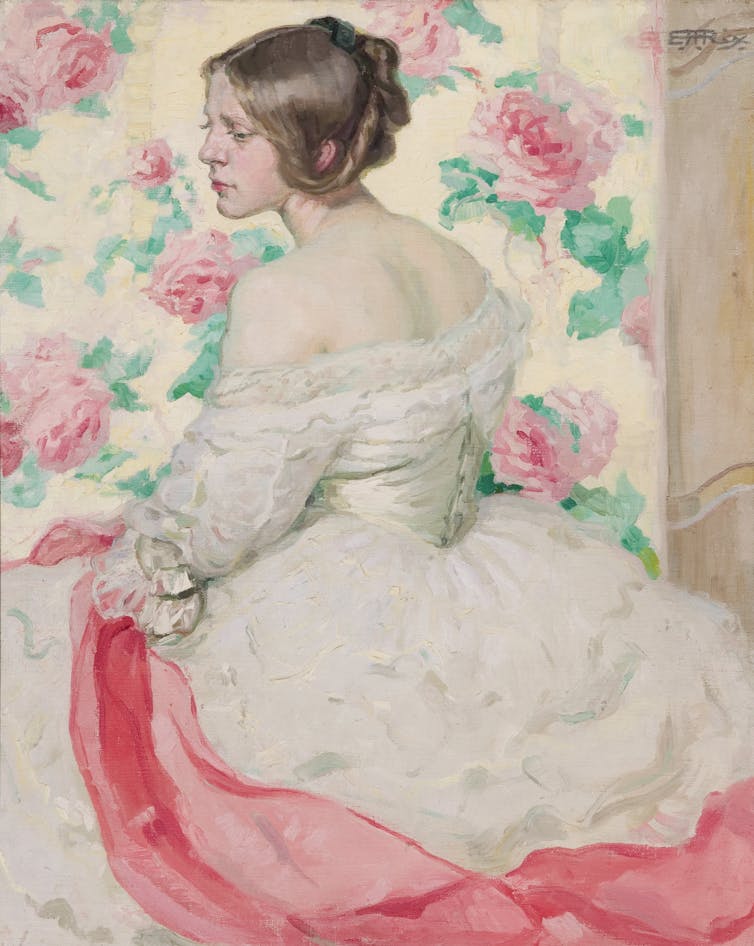 A woman sits in a white dress with a pink scarf.