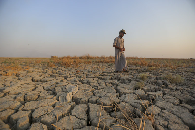 A man walks across a dried patch of land.