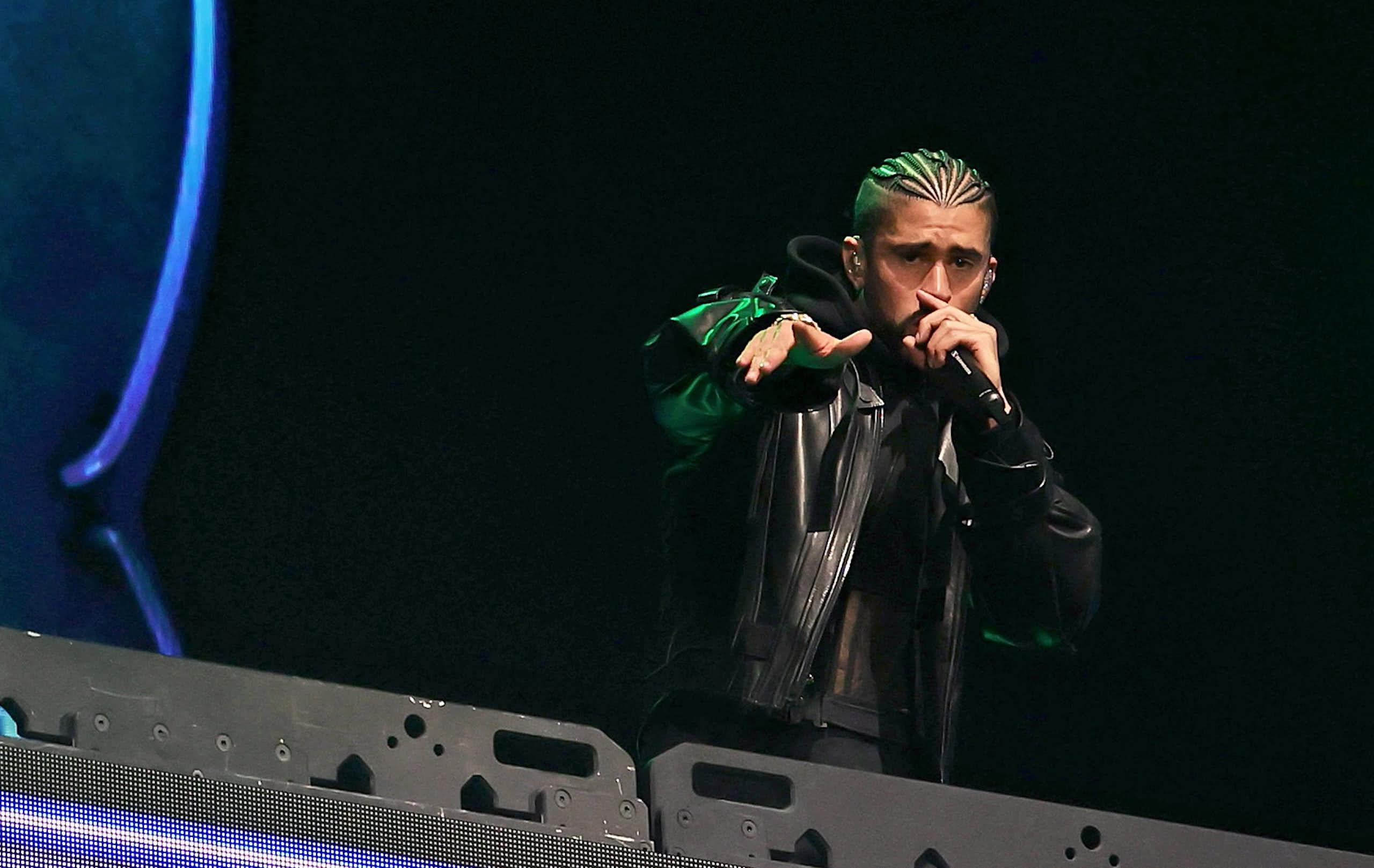 Man with dreadlocks raps into a microphone from a stage with an LED blue bunny head flashing in the background.