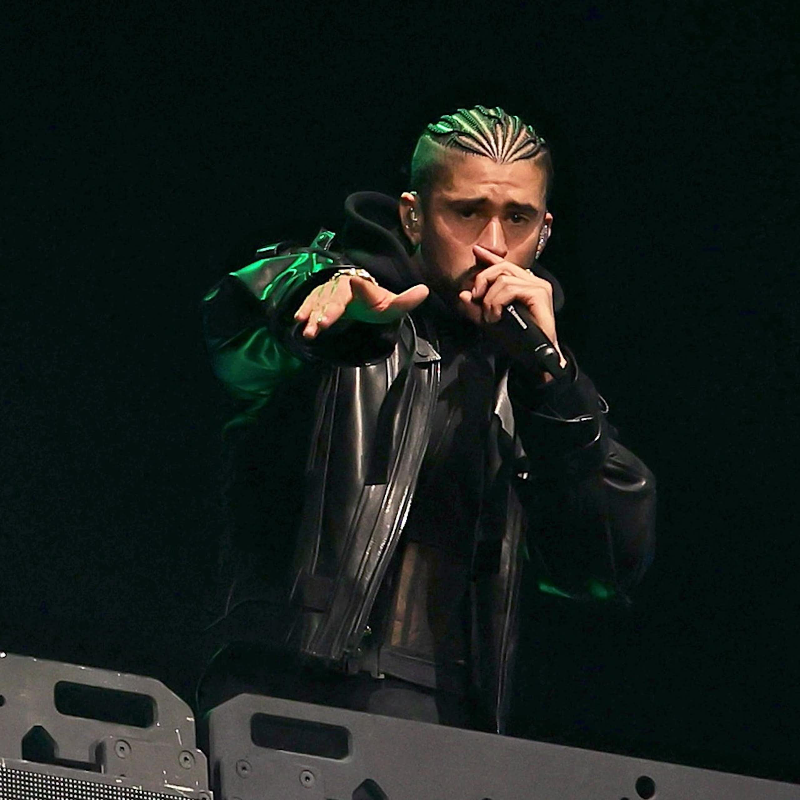 Man with dreadlocks raps into a microphone from a stage with an LED blue bunny head flashing in the background.